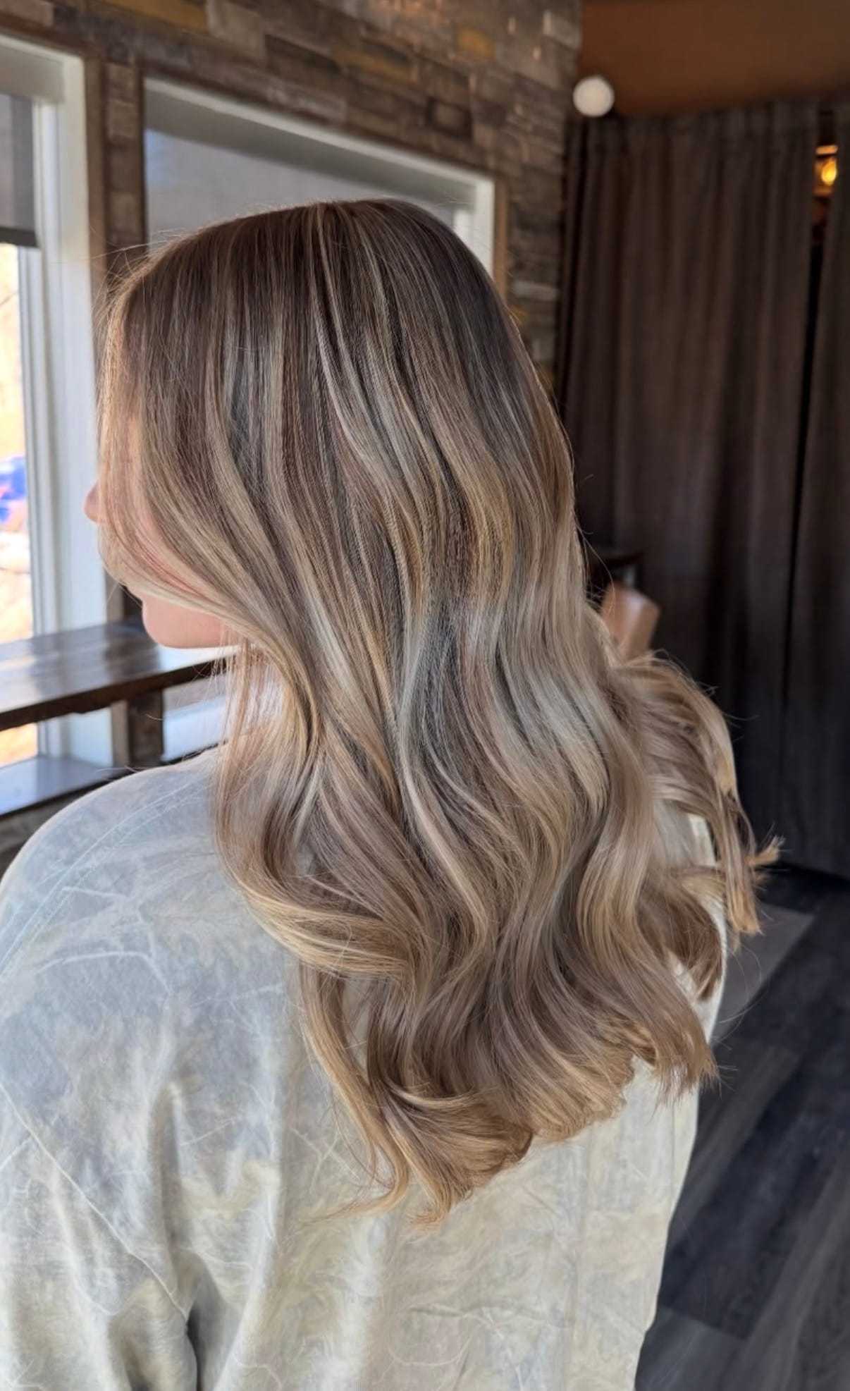 Blonde hair with brown highlights in soft, wavy style, viewed from the back indoors.